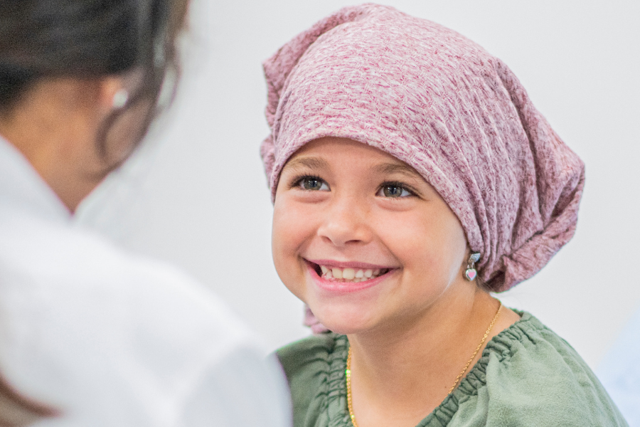 Young girl wearing a pink headscarf smiles at a healthcare professional during a medical visit outside a clinical setting? (informative alt)