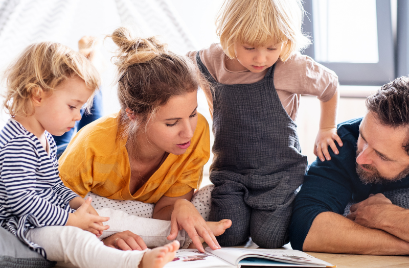 Family lying on the living room floor reading a book together.