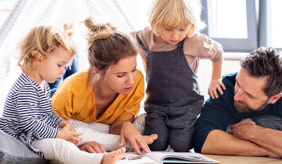 Family lying on the living room floor reading a book together.