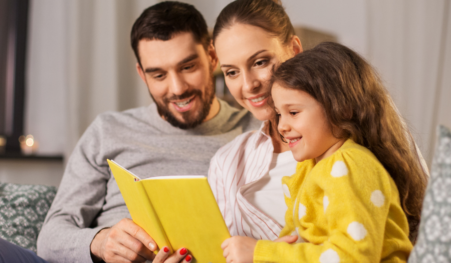 Family of three reading a yellow book together on a couch, smiling at the story.