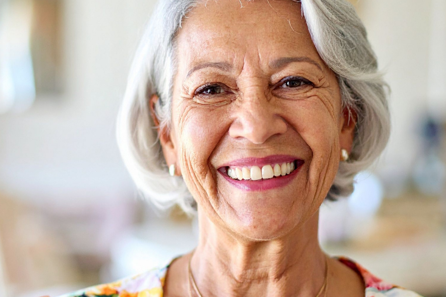 Smiling elderly woman with short gray hair in a bright indoor setting wearing a floral top.