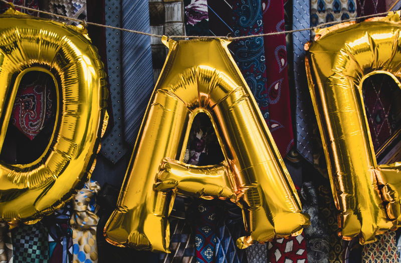 Gold foil balloons spell 'DAD' hanging over a display of colorful neckties.
