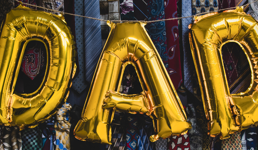 Gold foil balloons spell 'DAD' hanging over a display of colorful neckties.