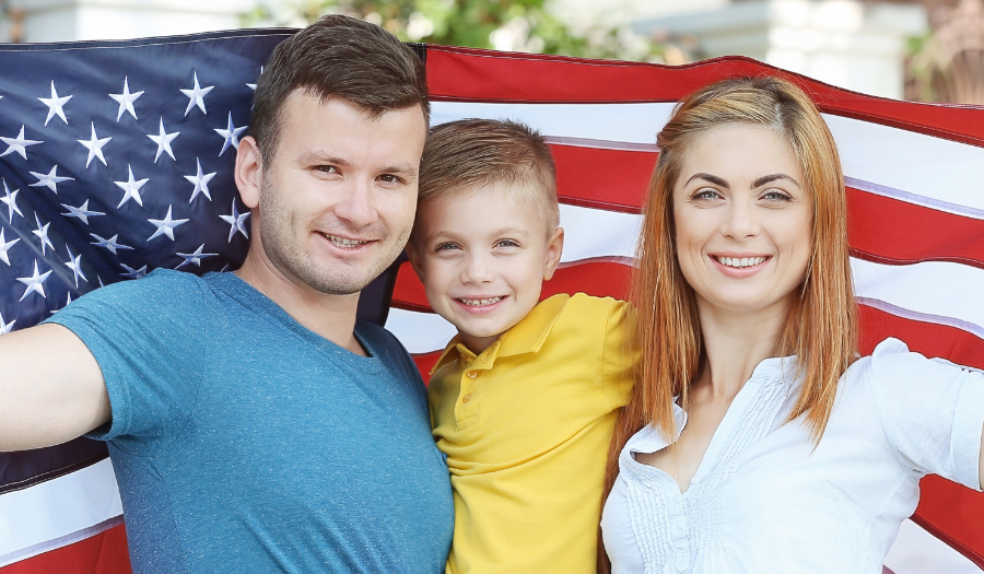AccuQuote Blog 2 - AccuQuote Family of three smiling, holding up a large American flag outdoors.