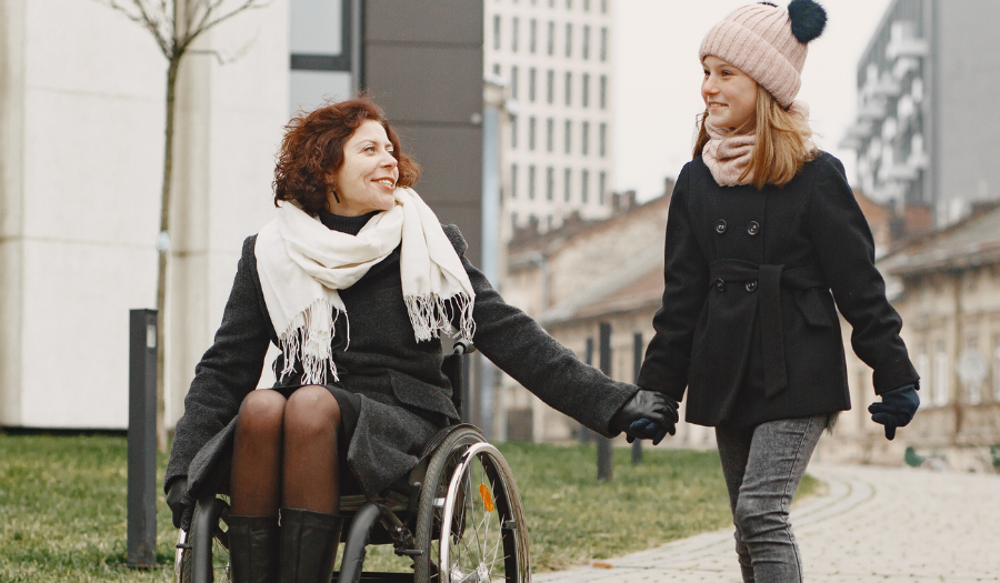 AccuQuote Blog 3 - AccuQuote Woman in a wheelchair and a girl walking hand in hand along a city path in winter.