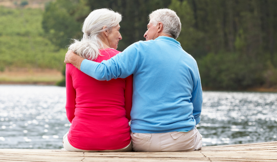 AccuQuote Blog 5 - AccuQuote Older couple sits on a wooden dock by a lake, with arms around each other, enjoying a quiet moment.