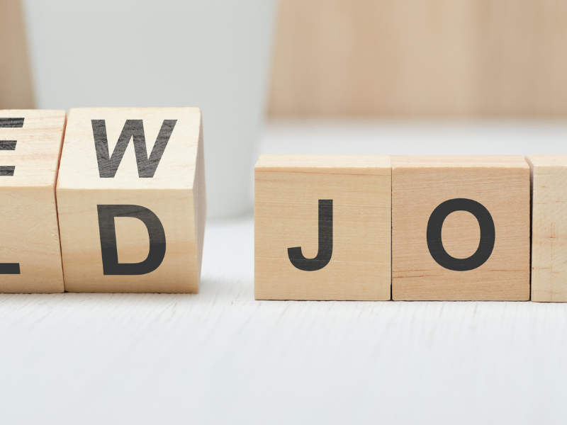 Wooden letter blocks spell ‘NEW OLD JOB’ on a light surface, suggesting a career change.